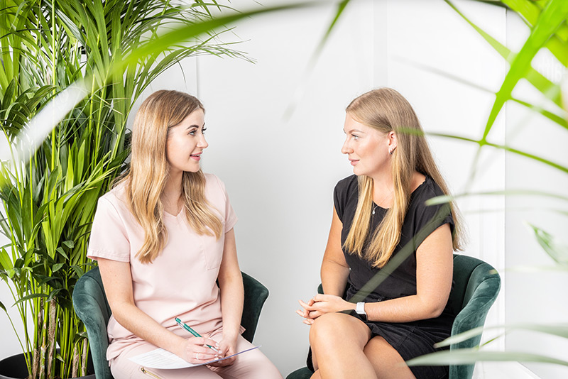 Aesthetic consultant and client chatting in a welcoming plant-filled room.