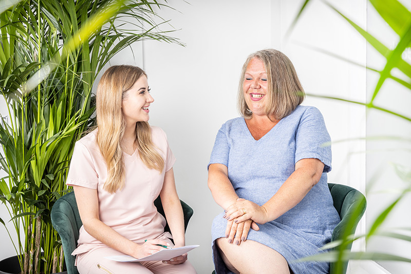 Aesthetic consultant and client chatting in a welcoming plant-filled room.